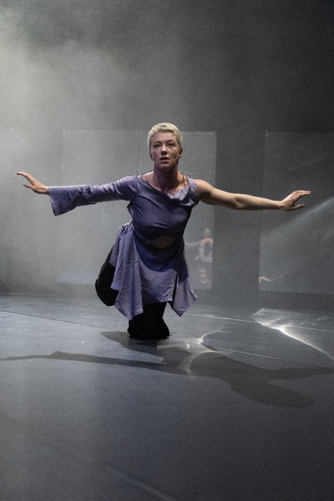 Performer kneeling on stage with arms outstretched in The Uprising